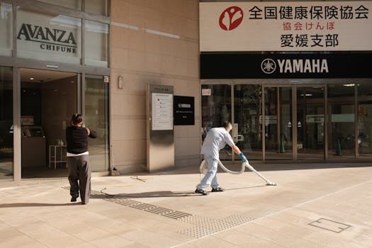 Two people clean the pavement outside a Yamaha building in Japan. Urban maintenance scene.